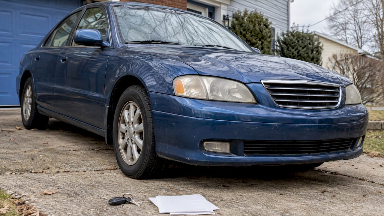 Blue sedan and estate sale paperwork on driveway